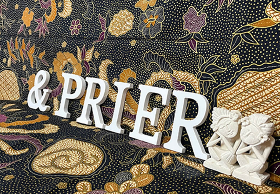 エキゾチックな模様の布を背景に、白い文字「&PRIER」と白い2体の座像が並んでいる